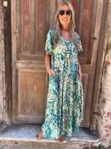 Vestido largo de seda, fluido y amplio, con mangas cortas y bolsillos laterales. Presenta un estampado en tonos turquesa y beige/crema.