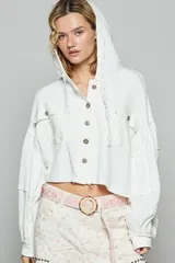 Campera corta blanca con textura waffle, capucha ajustable con cordones, cierre con botones al frente, bolsillos con solapa en el pecho y mangas amplias con puño elástico.