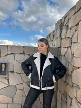 Campera gamulán negra con interior de piel sintética color crema, cierre cruzado con cremallera y cuello con solapas amplias.