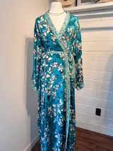 Kimono largo con estampado floral en tonos turquesa, blanco y rosa, con detalles geométricos en cuello, borde y cinturón.
