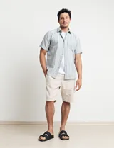 Camisa de manga corta a rayas verticales en tonos celeste, verde y blanco, con cuello clásico y bolsillo en el pecho. Cierre frontal con botones. Corte recto.