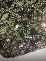 Vestido corto negro con bordados dorados y lentejuelas, escote en V profundo y breteles finos. Espalda descubierta.