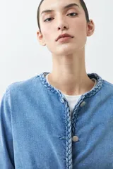 Chaqueta de jean celeste con cuello redondo, cierre con botones metálicos y detalle trenzado en cuello, bolsillos y ruedo.