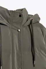 Anorak acolchado color verde oliva, resistente al viento y con aislamiento térmico. Tiene cuello alto con capucha ajustable con cordones, manga larga con puño interior, bolsillos delanteros con forro polar y cierre de cremallera, y cierre frontal con cremallera oculta y botones a presión.