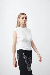 Top sin mangas color beige, confeccionado en tejido acanalado. Presenta hombreras definidas y un recorte fruncido bajo el busto que ajusta la silueta.