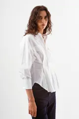 Camisa blanca de manga larga con cuello mao, corte holgado y detalles de bolsillos superpuestos en el pecho.