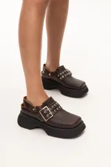 Zueco de cuero marrón con diseño contemporáneo y suela gruesa, ideal para combinar con diversos atuendos.