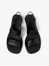 Sandalias de cuero vacuno color negro, con dos tiras anchas sobre el empeine, tira trasera con hebilla ajustable y suela baja con pequeño taco cuadrado.