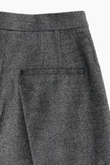Pantalón sastrero gris con cintura elástica de tiro alto, cierre y pretina prolongada con botón. Modelo con bolsillos al bies, solapa decorativa con botón adelante y bolsillos de atrás insertados. Piernas amplias con pinzas y pliegues adelante y atrás.