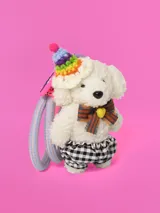 Llavero con forma de oso de peluche blanco con gorro de fiesta tejido a crochet con pompon y moño a rayas. El llavero tiene dos cintas elásticas para sujetar el pelo.