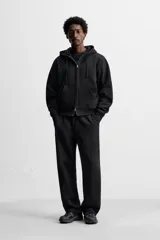 Sudadera negra relaxed fit de algodón compacto con interior en rizo, cuello con capucha ajustable, manga larga, bolsillos frontales tipo canguro, acabados en rib y cierre frontal con cremallera.