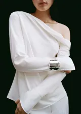 Blusa color crudo de tejido satinado, con cuello drapeado, mangas largas con puños abiertos y corte recto. Ideal para eventos formales.