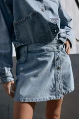 Falda pantalón de tiro alto de denim celeste con efecto lavado y roturas frontales. Tiene cinco bolsillos y cierre frontal con cremallera oculta y botones.