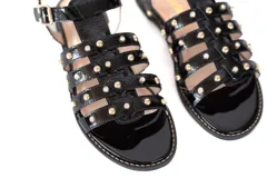 Sandalias negras de charol con tachas doradas y hebilla lateral.