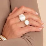 Anillo de plata 925 con baño de oro, engaste circular con piedra central de nácar blanco. El aro tiene detalles estriados en el engaste.