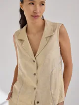 Camisa color beige de lino y rayon, sin mangas, con cuello camisero, cierre frontal con botones y detalle de vivos plateados en los bordes.