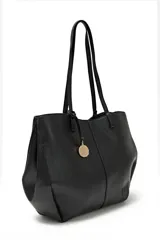 Cartera tote negra de cuero sintético con doble asa de hombro y dije metálico circular con el nombre de la marca.