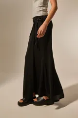 Falda larga negra con detalle de nudo lateral y tiras colgantes, de corte ajustado en la parte superior y ligeramente acampanado en el ruedo.
