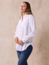 Camisa blanca de lyocell, marca Hester & Orchard. Tiene cuello con solapa, abertura central con botones, bolsillo aplicado en el pecho y ruedo desflecado.