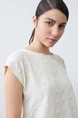 Blusa color beige con textura de lunares en relieve, cuello redondo y mangas cortas.