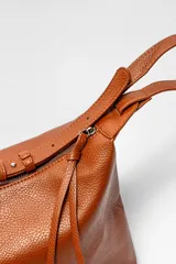 Bolso tipo hobo de cuero sintético color rojo oscuro con textura granulada.