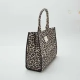 Bolso shopper con estampado de leopardo en tonos beige y negro, con asas cortas y etiqueta con texto en el frente.