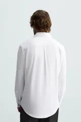 Camisa color beige de corte slim fit, confeccionada en tejido elástico que minimiza las arrugas. Tiene cuello italiano abierto, manga larga con puños abotonados y cierre frontal con botones.