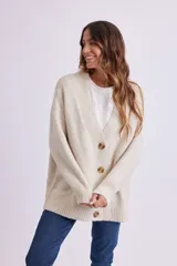 Cardigan de punto color crema, con escote en V, cierre frontal con botones marrones y corte holgado.