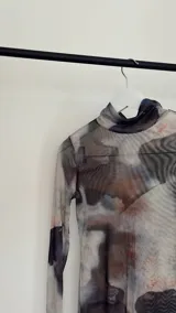 Minivestido de microtul elastizado con estampado abstracto en tonos grises y marrones. Tiene cuello alto, mangas largas acampanadas y abertura lateral en la falda.