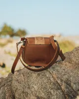 Bandolera de cuero color marrón con correa larga regulable, solapa con diseño trenzado y cierre con broche imantado.