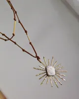 Collar con dije de bronce con forma de sol y centro de nácar, engarzado en un cordón de cuero marrón con detalles de bronce.