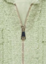 Chaqueta corta de tweed color verde claro, con cuello redondo, cierre frontal con cremallera y cuatro bolsillos de parche en la parte delantera.