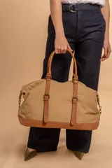 Bolso de viaje color beige, confeccionado en tela canvas con detalles en símil cuero color marrón. Incluye asas dobles y correa ajustable para llevar al hombro o cruzado.