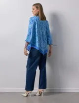 Blusa de gasa estampada marca Ruby Rd, de color azul. Tiene cuello a la base, escote en V y abertura central con botones. La delantera es plisada. Las mangas son ¾ con frunce. El ruedo y la espalda son asimétricos.