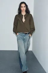 Camisa blanca de popelina con cuello solapa, manga larga abullonada con puño y bajo recto. Cierre frontal con botones ocultos por solapa.