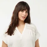 Blusa blanca de doble gasa de algodón con escote en V y detalle de encaje en los hombros.