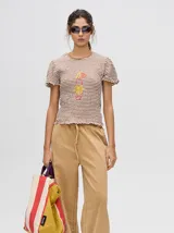 Mono largo de jean celeste con corte holgado, cintura elastizada con cordón ajustable, sin mangas, cuello camisero y cierre frontal con botones. Presenta bordados de motivos playeros en el pecho.