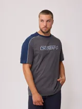 Remera gris de hombre con mangas cortas azul marino, corte en hombro/manga con línea blanca y estampado frontal con el logo de la marca Rusty en azul y blanco.