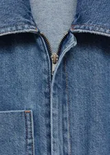 Mono largo de denim azul con cuello camisero, mangas cortas y cierre frontal con cremallera oculta. Incluye cinturón ajustable con hebilla metálica y bolsillo de parche en el pecho.