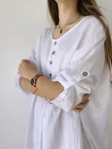 Vestido blanco de lino, corte holgado, con cuello redondo, mangas 3/4 con abertura y botones en el frente.