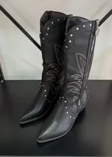 Botas texanas negras de caña alta con bordados en color blanco y tachas plateadas. Cierre lateral con cremallera.