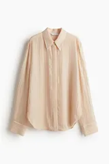 Camisa color piel de manga larga en gasa transparente con strass brillante. Modelo con cuello de pico, tapeta con botones ocultos y canesú de doble capa en la espalda. Puños abotonados y bajo redondeado.