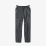 Pantalón de jogging negro con estampado de monogramas geométricos en gris y blanco. Tiene corte recto, cintura con cordón ajustable, bolsillos laterales y logo de cocodrilo bordado en el muslo.