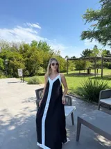 Vestido largo negro con breteles finos blancos, escote en V y corte recto. Presenta una franja vertical blanca en el centro.