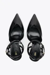 Zapato de tacón destalonado color negro charol, con tira trasera con hebilla y cierre con doble tira ajustable al tobillo.