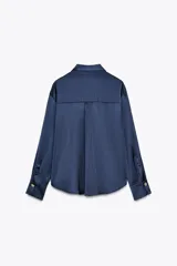 Camisa azul marino de satén con cuello solapa y manga larga. Cierre frontal con botones ocultos por solapa y botones dorados con relieve.