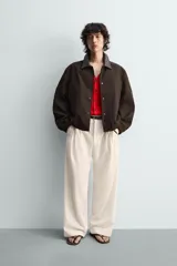 Cazadora de algodón con estructura canvas, color marrón oscuro, de corte relajado. Presenta cuello solapa de cuero negro, cierre frontal con botones a presión, bolsillos de vivo en cadera y puños y bajo elásticos.