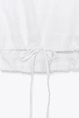 Camiseta blanca de algodón con cuello redondo, mangas cortas y bajo asimétrico ajustable con lazadas.