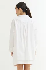 Camisa blanca de corte amplio, con cuello clásico, cierre frontal con botones y mangas largas con puños abotonados.
