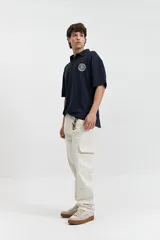 Remera polo color beige con textura acanalada, corte oversize, cuello clásico con botones y logo estampado en el pecho.